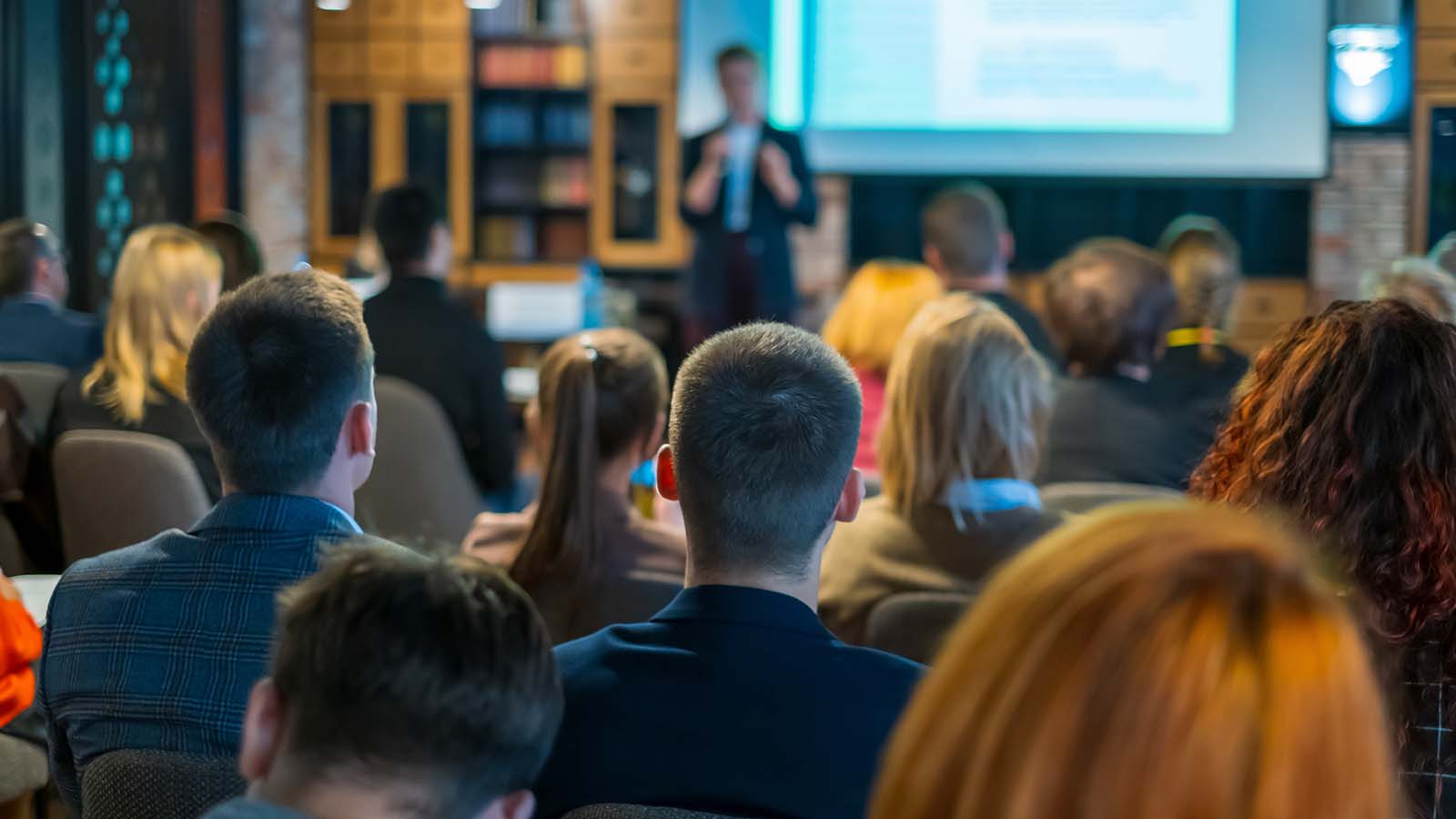 Rear view of an audience at a workshop listening to someone speak